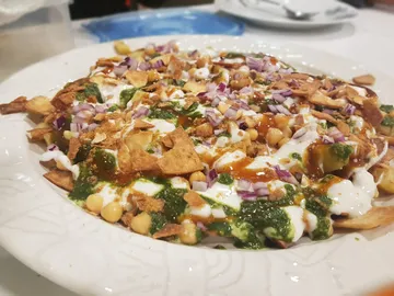 A plate of chaat topped with yoghurt and herbs.