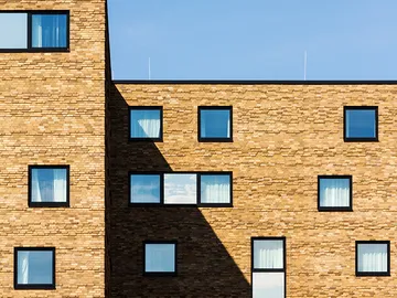 Brick façade with window, cast shadows, clear sky.