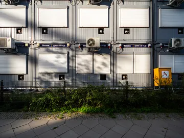 Grey wall with closed shutters and air conditioners.