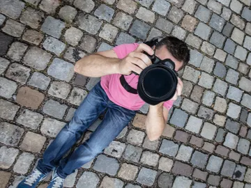 Mann fotografiert auf einem Kopfsteinpflasterweg, liegend.