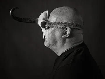Mann mit einem Tierkopf und Seilband trägt Maske.