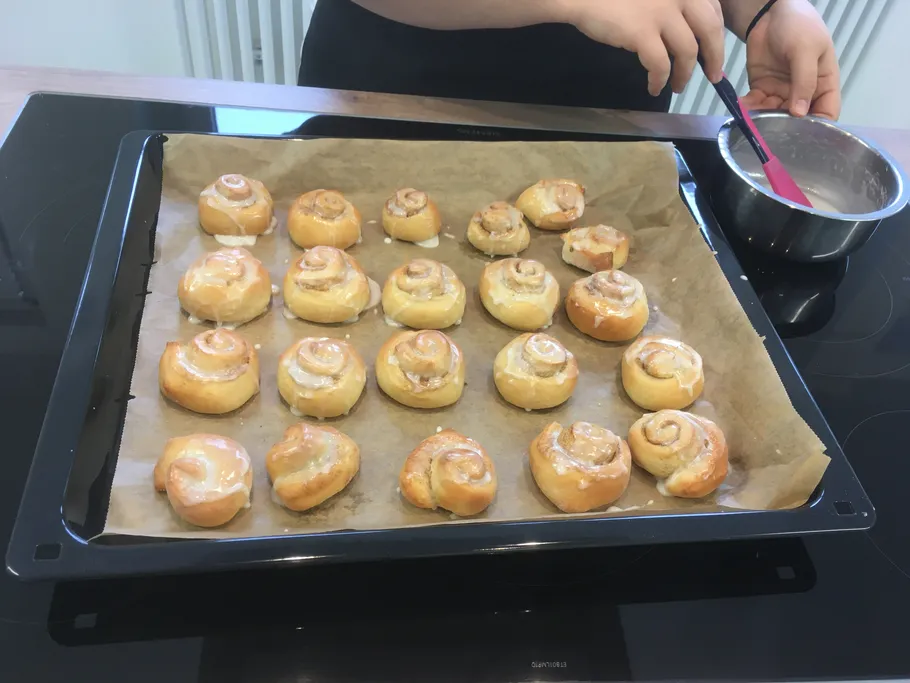 Person, die Zimtschnecken auf einem Backblech glasiert.