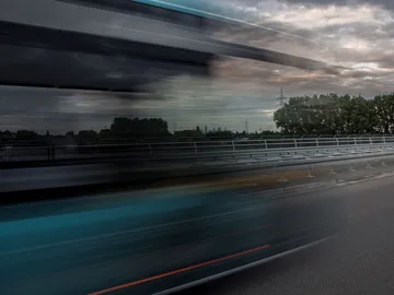 Schnell fahrender Bus auf einer Straße unter bewölkten Himmel.
