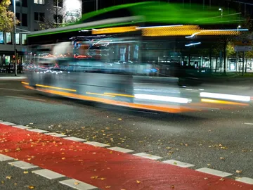 Bus fährt schnell über eine rote Fahrbahn bei Nacht.