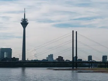 Düsseldorf TV Tower stands next to a bridge on the water.