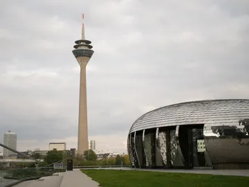 Fernseh-Turm steht neben modernem, glänzendem Gebäude unter Wolken.