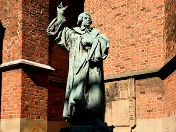 Bronze statue raises hand in front of red brick.