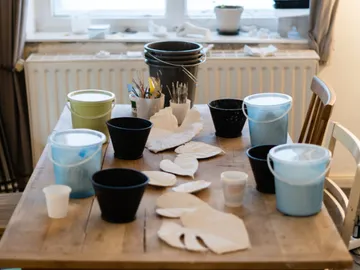 Tisch mit Farbtöpfen, Pinsel und Bastelmaterialien.