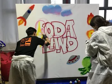 Zwei Personen sprayen bunte Grafiken auf eine Leinwand.