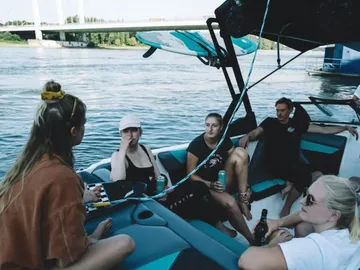 Gruppe entspannt auf einem Boot, Getränken genießend, Wasserfläche.