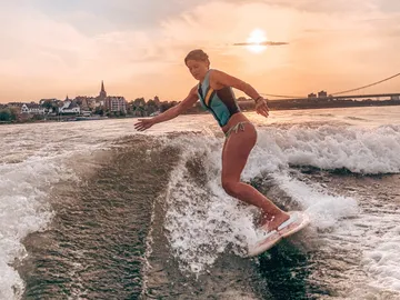 Eine Frau surft auf einer Welle bei Sonnenuntergang.