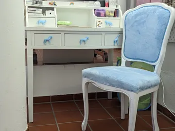 Weißer Tisch mit blauen Pferdegriffen und gepolsterter Stuhl.