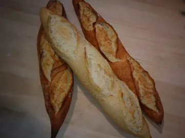 Drei Baguettes liegen auf einem Holzbrett.
