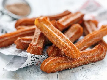 Frittierte Churros liegen auf Zeitungspapier, bestreut mit Zucker.