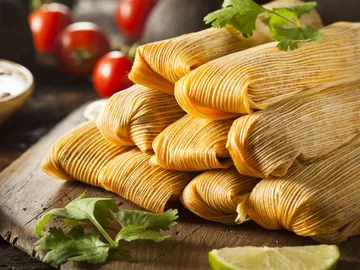 Gestapelte Tamales auf einem Holzbrett mit frischen Zutaten.