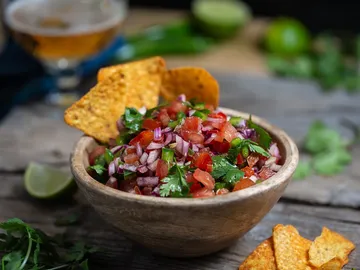 Schüssel mit Salsa, begleitet von Tortilla-Chips, auf Holzoberfläche.