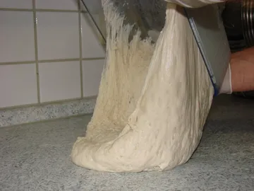 Teig wird aus einer Schüssel gezogen, in einer Küche.