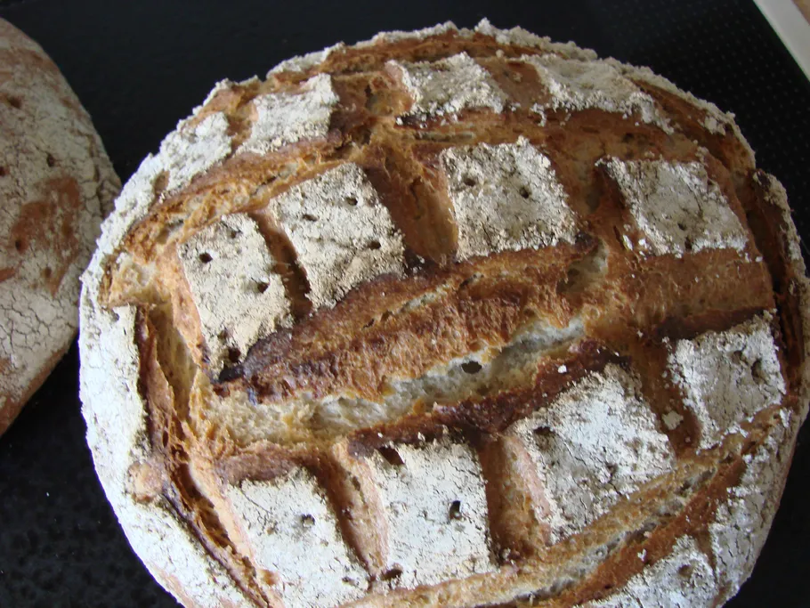 Round loaf of bread is lying on a black background, rustic.