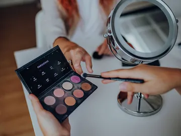 Augenmakeup-Palette wird mit Pinsel vor Spiegel benutzt.