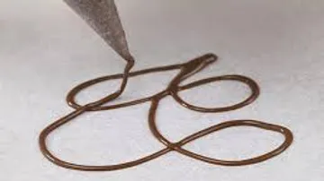 Chocolate cake draws curved lines on white paper.