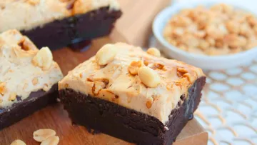 Schokoladenbrownie mit Erdnussbuttercreme, im Hintergrund Erdnüsse.