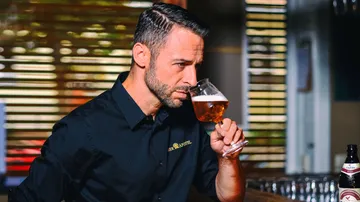 Man reviews beer in a bar with wooden blinds.