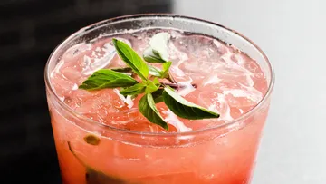 A glass of cocktail with ice, mint and red drink.