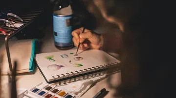 Eine Hand malt Aquarelle in einem Skizzenbuch.