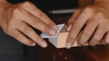 Hands grind a piece of wood on a workbench.