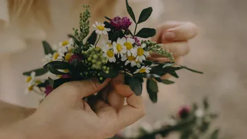 Hände formen einen Blumenkranz mit bunten Blumen.