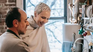 Two people smile and interact in a kitchen.