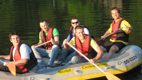 Five men are happily paddling in an inflatable boat.