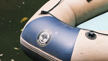 Inflatable boat floats calmly in water surrounded by leaves.