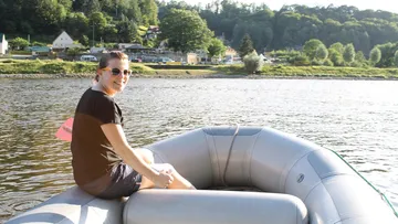 Person sitzt im Schlauchboot und lächelt am Wasser.