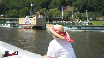 Eine Frau sitzt auf einem Boot und schaut ein Dampfschiff an.