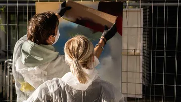 Two people spray paint onto an outdoor canvas.