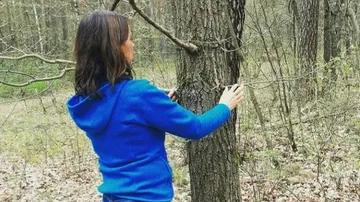 Woman hugs a tree in the woods while walking.