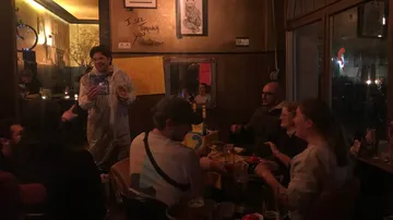 Person in Schutzanzug spricht vor Publikum in einem Café.
