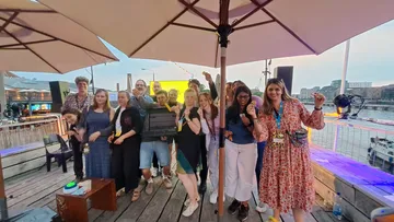 Gruppe von Menschen posiert fröhlich unter Sonnenschirmen am Wasser.