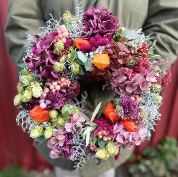 A flower wreath in bright colors is held by one person.