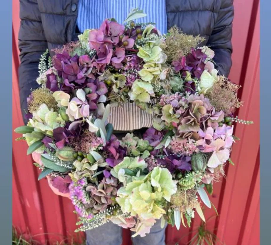 Person holding colorful hydrangea wreath outdoors.