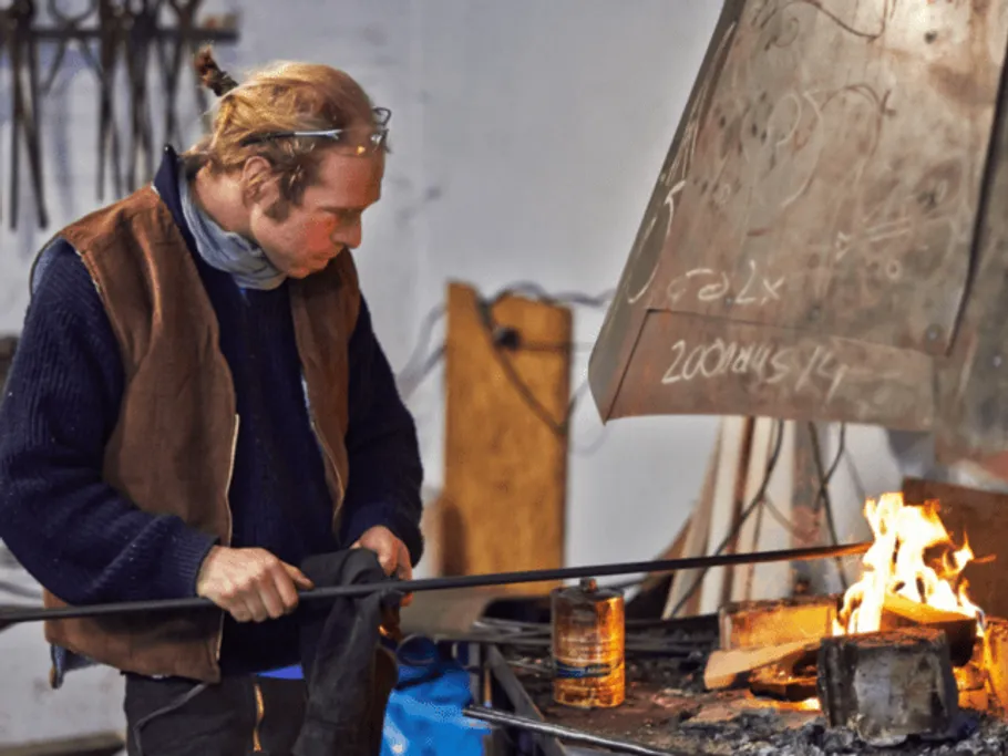 Blacksmith works on glowing metal on fire in the workshop.