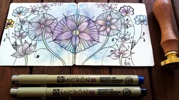 Bunt gezeichnete Blumen in einem offenen Skizzenbuch, Stifte daneben.