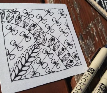 Mandala mit floralen Mustern auf hellem Papier, daneben Stifte.