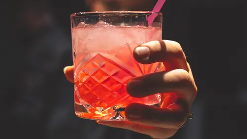 Ein Cocktailglas wird mit einer Hand gehalten, rot gefärbt.
