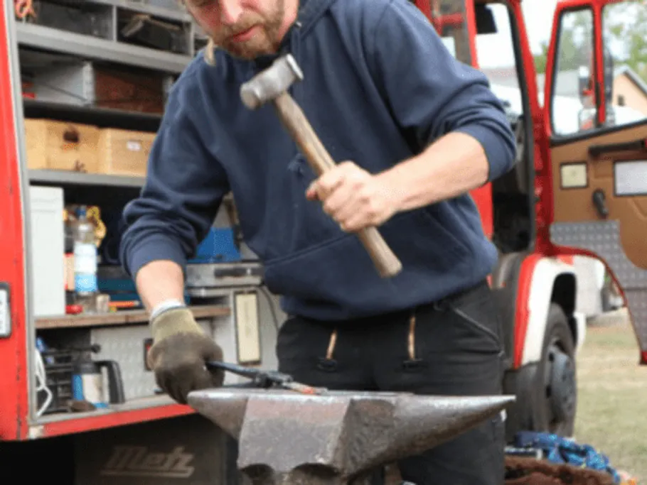 Schmied schlägt mit Hammer auf Amboss in freier Natur.