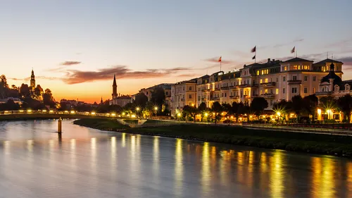 River reflects evening city lighting under a sunset.