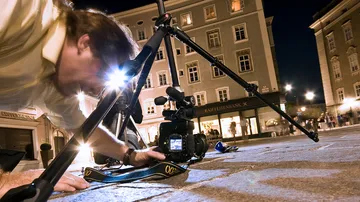 Fotograf positioniert Kamera auf Stativ in einer Stadt bei Nacht.