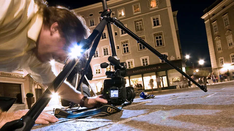 Photographer positions camera on tripod in a city at night.