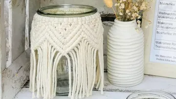 Glass jar with macrame decoration stands next to a vase.